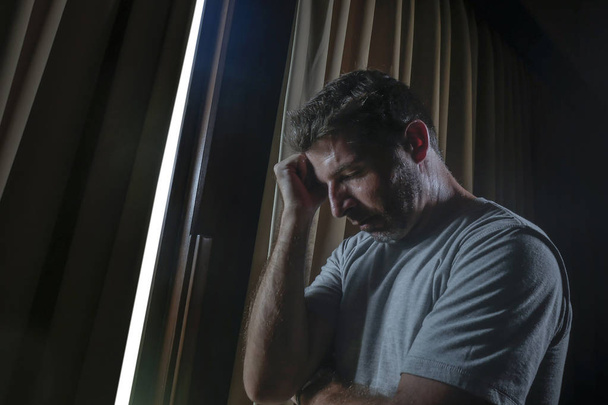 dramatische licht binnenshuis portret van triest en depressief aantrekkelijke jongeman op thuis kijken door kamer raam doordachte en nadenkend verloren in pijn lijden depressie probleem hart gebroken - Foto, afbeelding