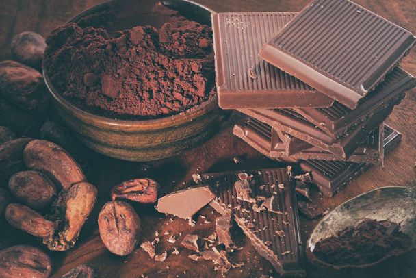 Chocolate negro roto, cacao en polvo y granos de café en una mesa de madera
 - Foto, imagen