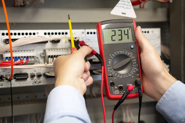 Electrician adjusts electrical control panel on power station, using tester. - Fotó, kép