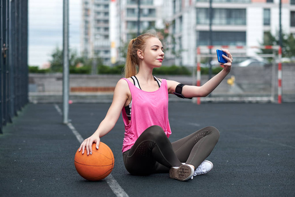 Giovane donna con pallacanestro utilizzando il telefono dopo l'allenamento, facendo selfie. - Foto, immagini