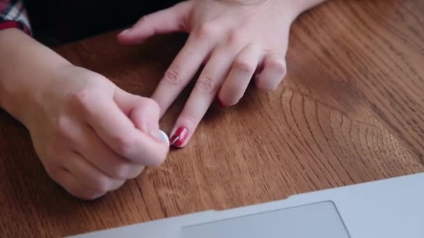 Een mooie zakenvrouw zit aan een tafel met een laptop in een café en schildert haar nagels. - Video