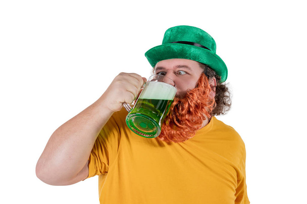 Χαμογελαστά ευτυχισμένος λίπος άνθρωπος σε ένα καπέλο καλλικάτζαρος με πράσινο μπύρα. Αυτός γιορτάζει Αγίου Πατρικίου - Φωτογραφία, εικόνα