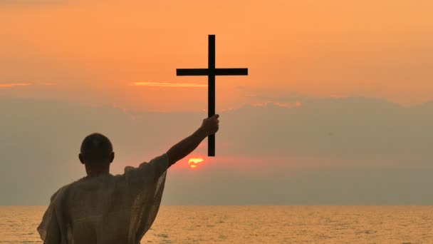 4. Cristiano hombre de oración asceta, monje tomar cruz contra el atardecer en la costa
 - Metraje, vídeo