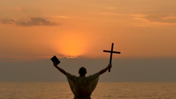 4. クロス禁欲的な修道士取ると seacost のオレンジ色の夕日に聖書を男します。キリスト教のチーム - 映像、動画