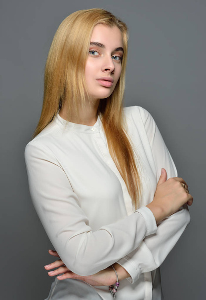 Portrait of the beautiful blonde woman with long hair in white blouse. Studio shooting with grey background. Natural make-up. - Фото, изображение