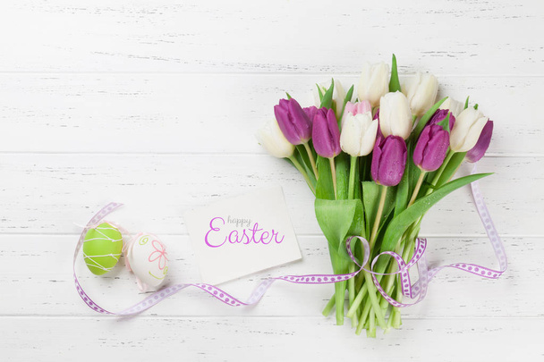 Pasen-wenskaart met tulp bloemen boeket en Pasen eieren. Bovenaanzicht over witte houten tafel met ruimte voor uw groeten - Foto, afbeelding