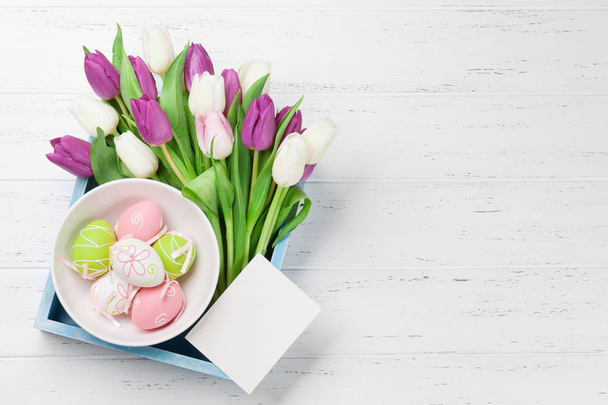 Easter greeting card with tulip flowers bouquet and easter eggs. Top view over white wooden table with space for your greetings - Foto, imagen