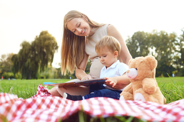 Mother with child reads on the grass in the park.  - Zdjęcie, obraz