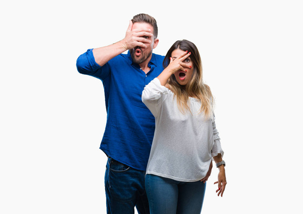 Young couple in love over isolated background peeking in shock covering face and eyes with hand, looking through fingers with embarrassed expression. - Foto, Bild