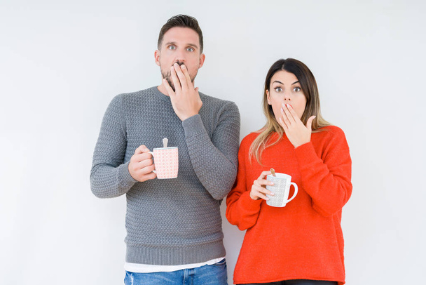 junges Paar trinkt Tasse Kaffee über isoliertem Hintergrunddeckel Mund mit vor Scham geschockter Hand für Fehler, Ausdruck von Angst, Angst in der Stille, geheimes Konzept - Foto, Bild