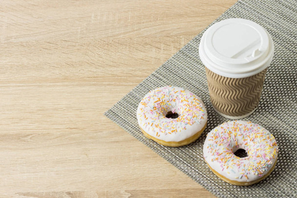 leckere, süße, frische Donuts und eine Papptasse mit Kaffee oder Tee auf einem hölzernen Hintergrund. Frühstückskonzept, Fast Food, Café, Bäckerei - Foto, Bild
