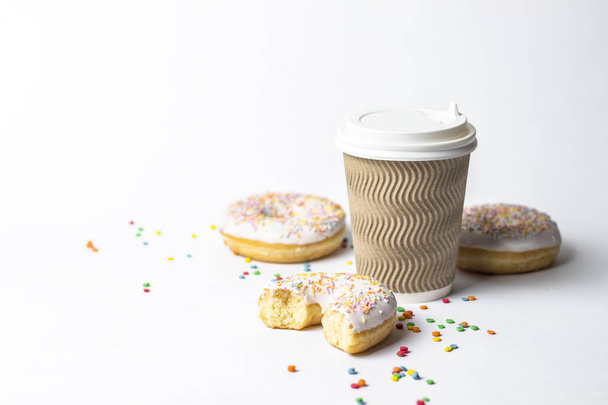 Паперова чашка з кришкою, кавою або чаєм, щоб піти і свіжими смачними пончиками і солодкими різнокольоровими декоративними цукерками на білому тлі. Концепція пекарні, свіжа випічка, смачний сніданок, фаст-фуд
 - Фото, зображення