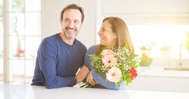 Romántica pareja de mediana edad sosteniendo flores enamoradas en casa
 - Foto, imagen