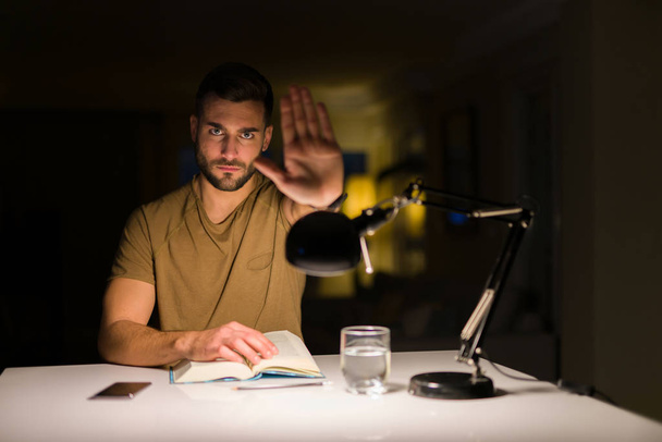 Young handsome student man studying at night at home with open hand doing stop sign with serious and confident expression, defense gesture - Foto, afbeelding