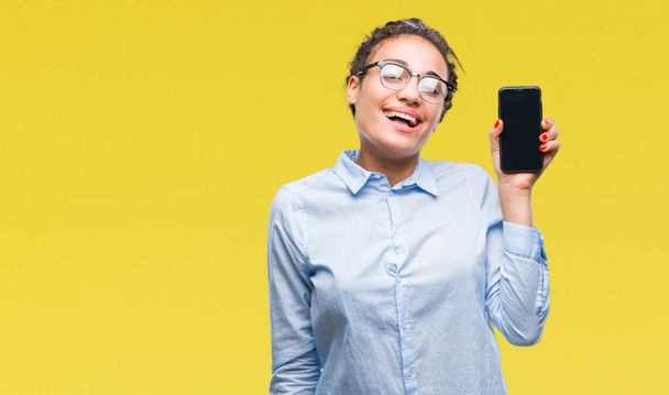 Молодые плетеные волосы африканская бизнес-девушка показывает экран смартфона на изолированном фоне с счастливым лицом стоя и улыбаясь с уверенной улыбкой показывая зубы
 - Фото, изображение