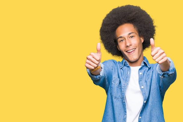 Jeune homme afro-américain aux cheveux afro approuvant faire un geste positif avec la main, le pouce levé souriant et heureux pour le succès. En regardant la caméra, geste gagnant
. - Photo, image