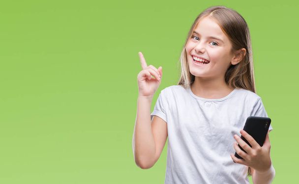 Jeune belle fille envoyer un message texte en utilisant smarpthone sur fond isolé très heureux pointant avec la main et le doigt sur le côté
 - Photo, image