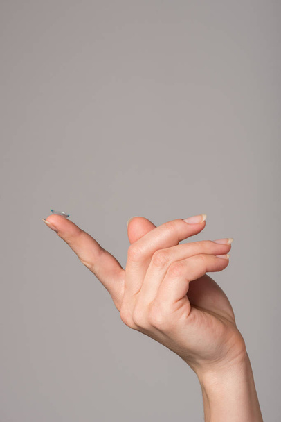 Мягкие контактные линзы лежат на пальце женской руки на сером фоне
 - Фото, изображение