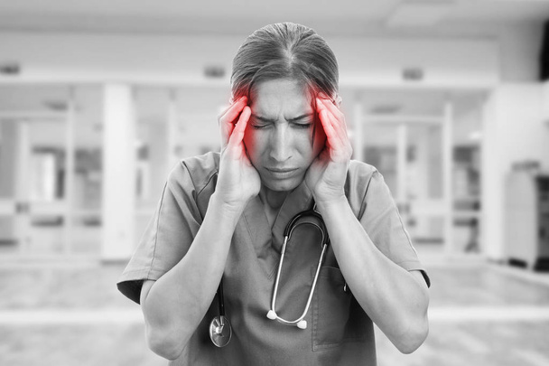 Black and white picture of nurse with headache holding hands on red coloured temples as pain concept - Photo, Image