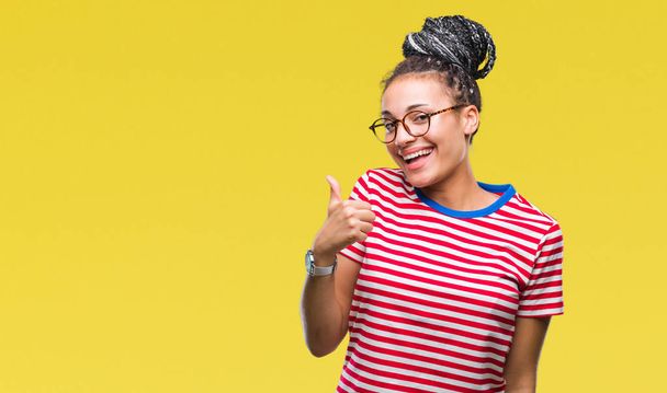 junge geflochtene Haare afrikanisches amerikanisches Mädchen mit Brille über isoliertem Hintergrund macht glückliche Daumen nach oben Geste mit der Hand. zustimmender Ausdruck, der mit Erfolg in die Kamera blickt. - Foto, Bild