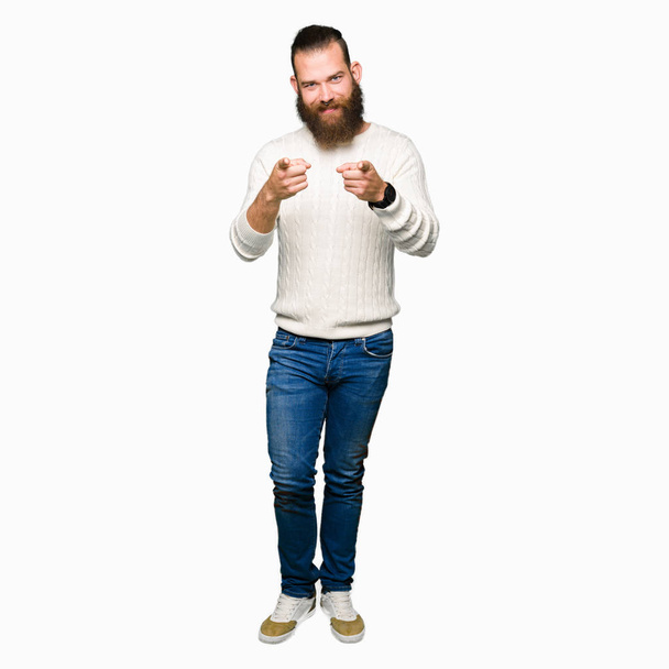 Молодий хіпстер у зимовому светрі вказує пальці на камеру з щасливим і смішним обличчям. Хороша енергія і вібрує
. - Фото, зображення