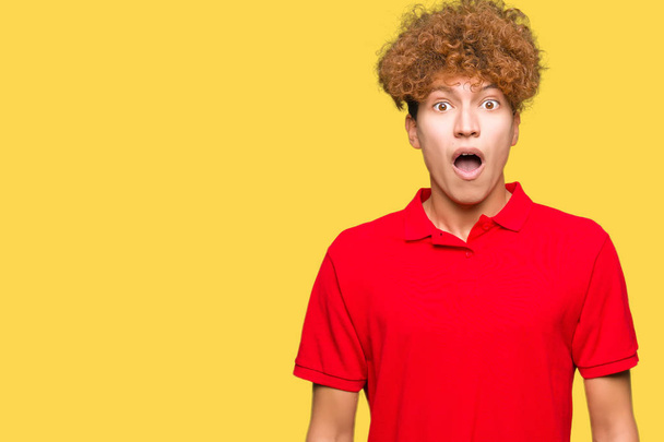 Młody przystojny mężczyzna z afro włosów na sobie czerwony t-shirt, boi się i wstrząśnięty wyrażenie zdziwienie, strach i podekscytowana twarz. - Zdjęcie, obraz