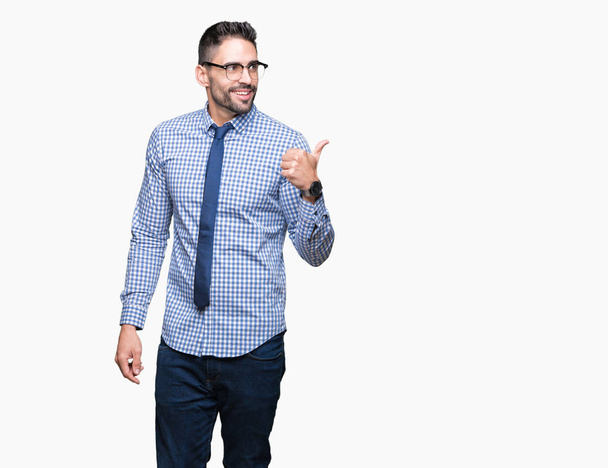 Giovane uomo d'affari indossa occhiali su sfondo isolato sorridente con volto felice guardando e indicando il lato con pollice in su
. - Foto, immagini