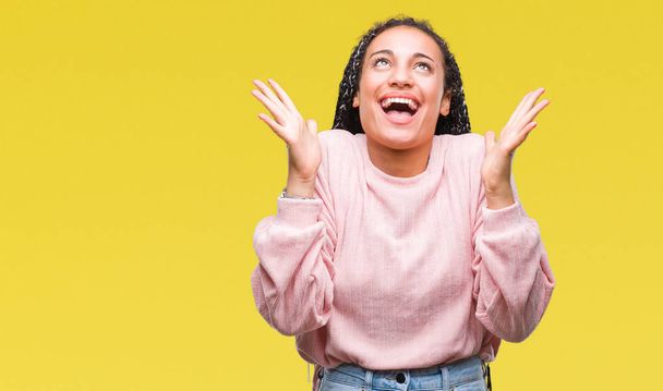 Young braided hair african american girl wearing sweater over isolated background celebrating crazy and amazed for success with arms raised and open eyes screaming excited. Winner concept - Photo, Image