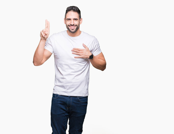 Hombre guapo con camiseta blanca sobre fondo blanco aislado Jurando con la mano en el pecho y los dedos, haciendo un juramento de lealtad promesa
 - Foto, Imagen