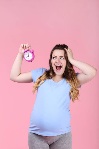 Beautiful pregnant woman with alarm clock on pink background - Foto, Bild