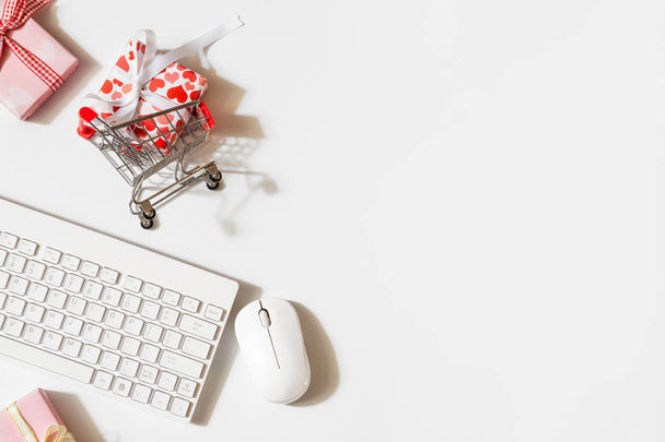 Overhead shot of wireless keyboard and mouse, gifts box with shopping cart. Flat lay top view office working space for Valentines' day and women's day shopping online concept. - Photo, Image