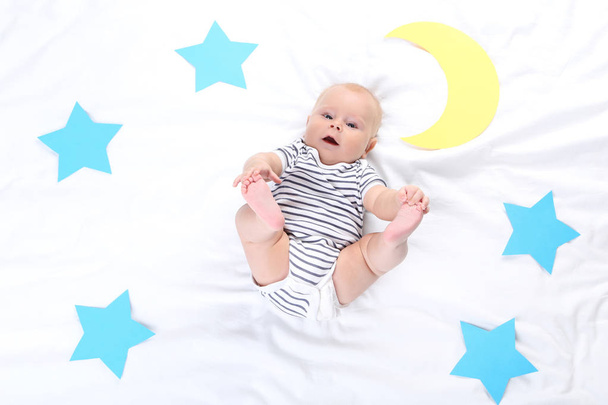 Baby boy with paper stars and moon lying on white bed - Fotó, kép
