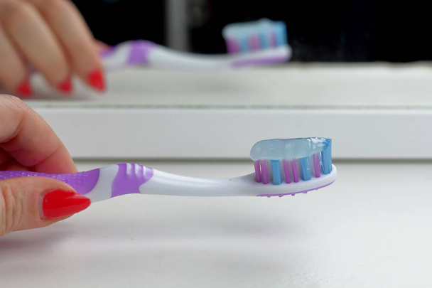 Spazzolino da denti rosa sullo scaffale bianco in bagno si riflette nello specchio, cura della mattina, cura dei denti e la salute nelle donne hande
 - Foto, immagini