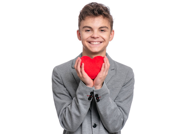 Happy Valentines Day. Cute young Teen Boy in Love with Red plush Heart in his hands. Smiling Child in grey suit, looking at camera, isolated on white background. - Foto, immagini