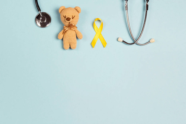 Childhood Cancer Awareness Yellow Ribbon with toy bear and stethoscope on blue background with copy space. Childhood Cancer Day February, 15. - Foto, afbeelding