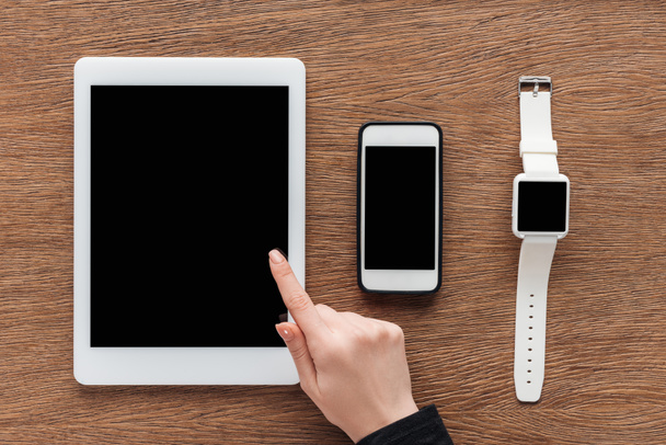 Vista ritagliata di donna con tablet digitale, smartphone e smartwatch con schermo bianco su sfondo di legno
 - Foto, immagini