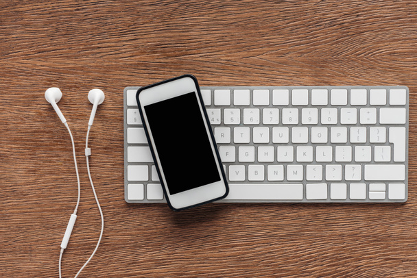 Pohled shora z klávesnice, smartphone s prázdnou obrazovkou a sluchátka na dřevěné pozadí - Fotografie, Obrázek