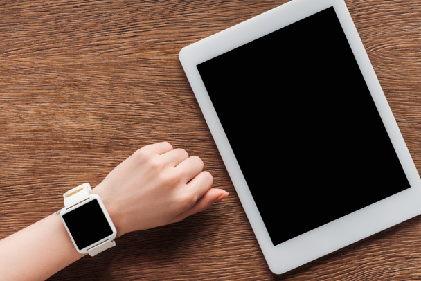 Vue partielle de la fille avec smartwatch et tablette numérique avec écran blanc sur fond en bois
 - Photo, image