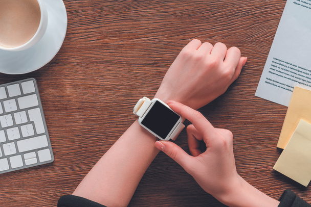Cropped view of girl using smartwatch with blank screen on wooden background - Foto, Imagen