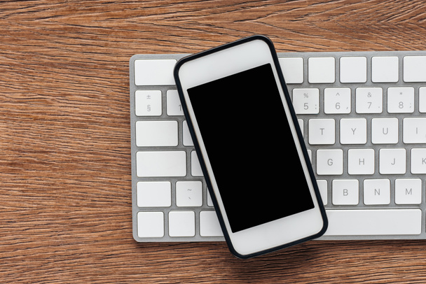 Top view of keyboard and smartphone with blank screen on wooden background - Photo, Image