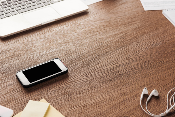Foto de smartphone con pantalla en blanco y auriculares en superficie de madera
 - Foto, Imagen