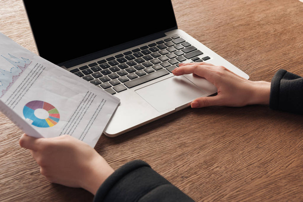 Cropped view of woman holding documents while using laptop with blank screen  - Foto, Imagem