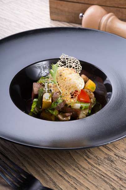 Salada de carne quente servida em um prato preto
 - Foto, Imagem