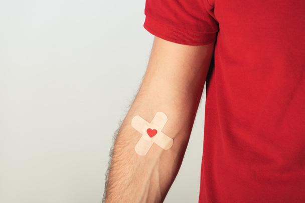 Vista parcial del paciente en camiseta roja con yeso sobre fondo gris, concepto de donación de sangre
 - Foto, Imagen