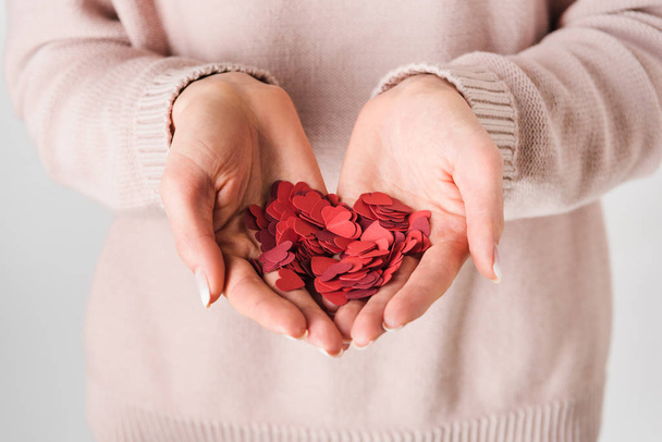 Partial view of woman in pink sweater holding paper hearts on grey background - Фото, зображення