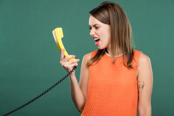 beautiful angry woman yelling at retro telephone isolated on green - Photo, Image