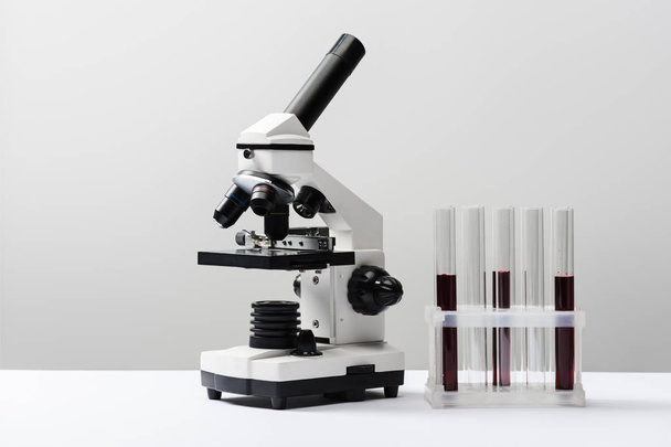 microscopio y tubos de ensayo con sangre sobre fondo gris
  - Foto, Imagen