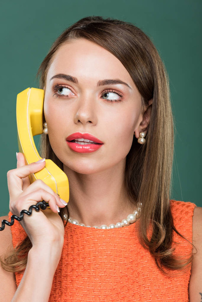 beautiful stylish woman looking away and talking on retro telephone isolated on green - Foto, imagen
