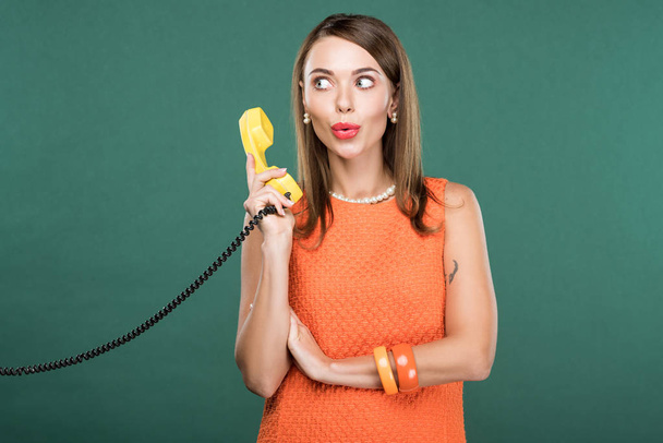 beautiful stylish woman pouting lips and holding retro telephone isolated on green - Foto, afbeelding