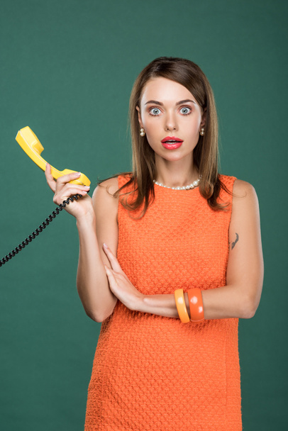 beautiful shocked woman holding retro telephone and looking at camera isolated on green - Foto, Imagem